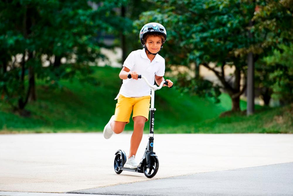 Мальчик в шлеме Micro Стикеры на самокате Micro Cruiser черный Мальчик в шлеме Micro Стикеры на самокате Micro Cruiser черный